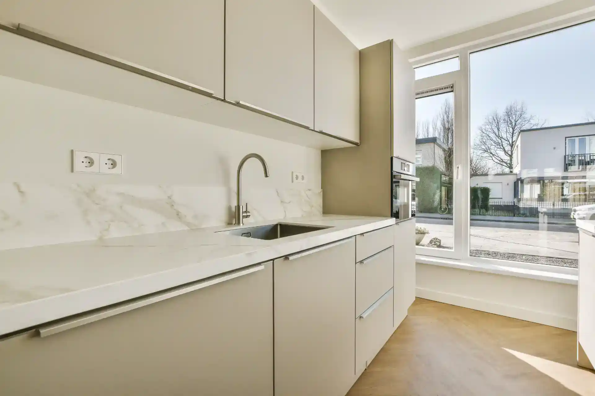 Lyst moderne køkken med lyse kabinetter og stor udendørs vinduesåbning, perfekt til hjemmet.