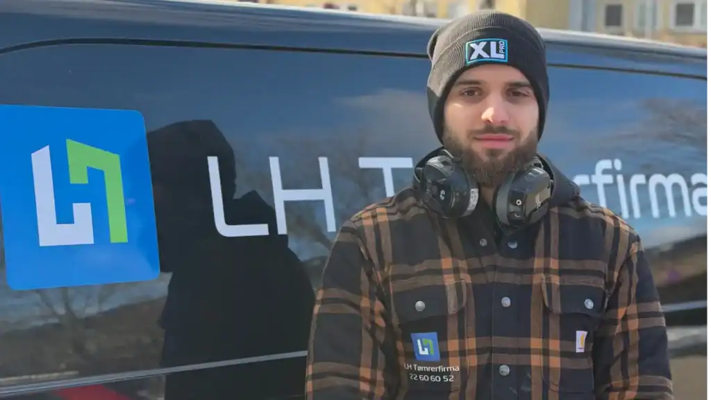 Mand med headset foran LHTømrerfirma ApS firmabil, klar til tømrerarbejde.